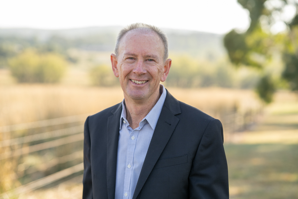 Man wearing a business suit standing in front of fence. 